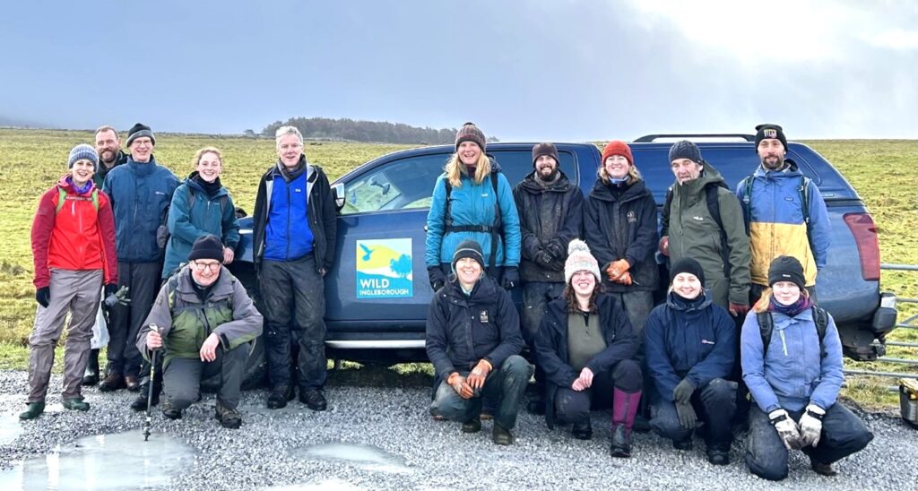 A group of people in a field next to an offroad vehicle with Wild Ingleborough branding