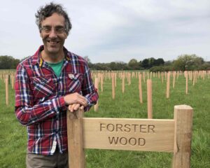 Piers Forster in a field of tree tubes, standing next to a sign that says Forster Wood